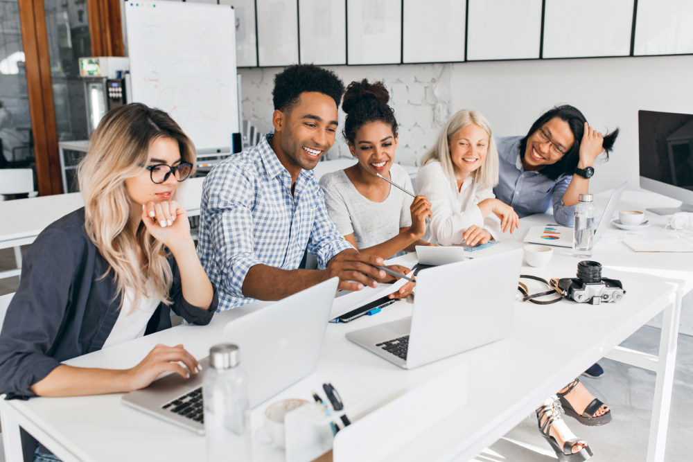 A group of people working together at a desk looking at a laptop